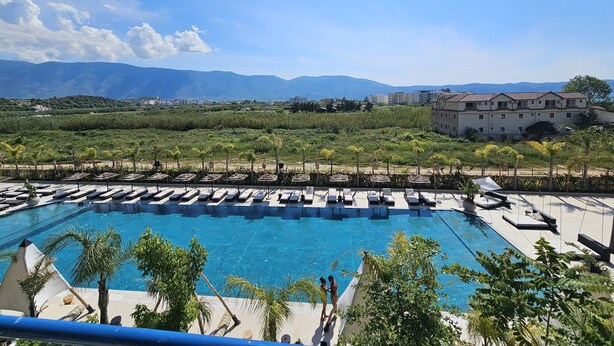 A swimming pool with lounge chairs, surrounded by greenery and mountains in the background. - Apartment With Pool View 001 (Orikum)