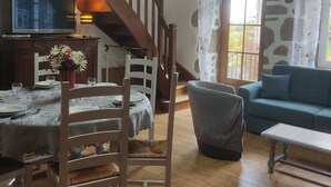 Un comedor con una mesa dispuesta para cuatro personas, una silla de madera, un sofá y un televisor sobre un mueble de madera.