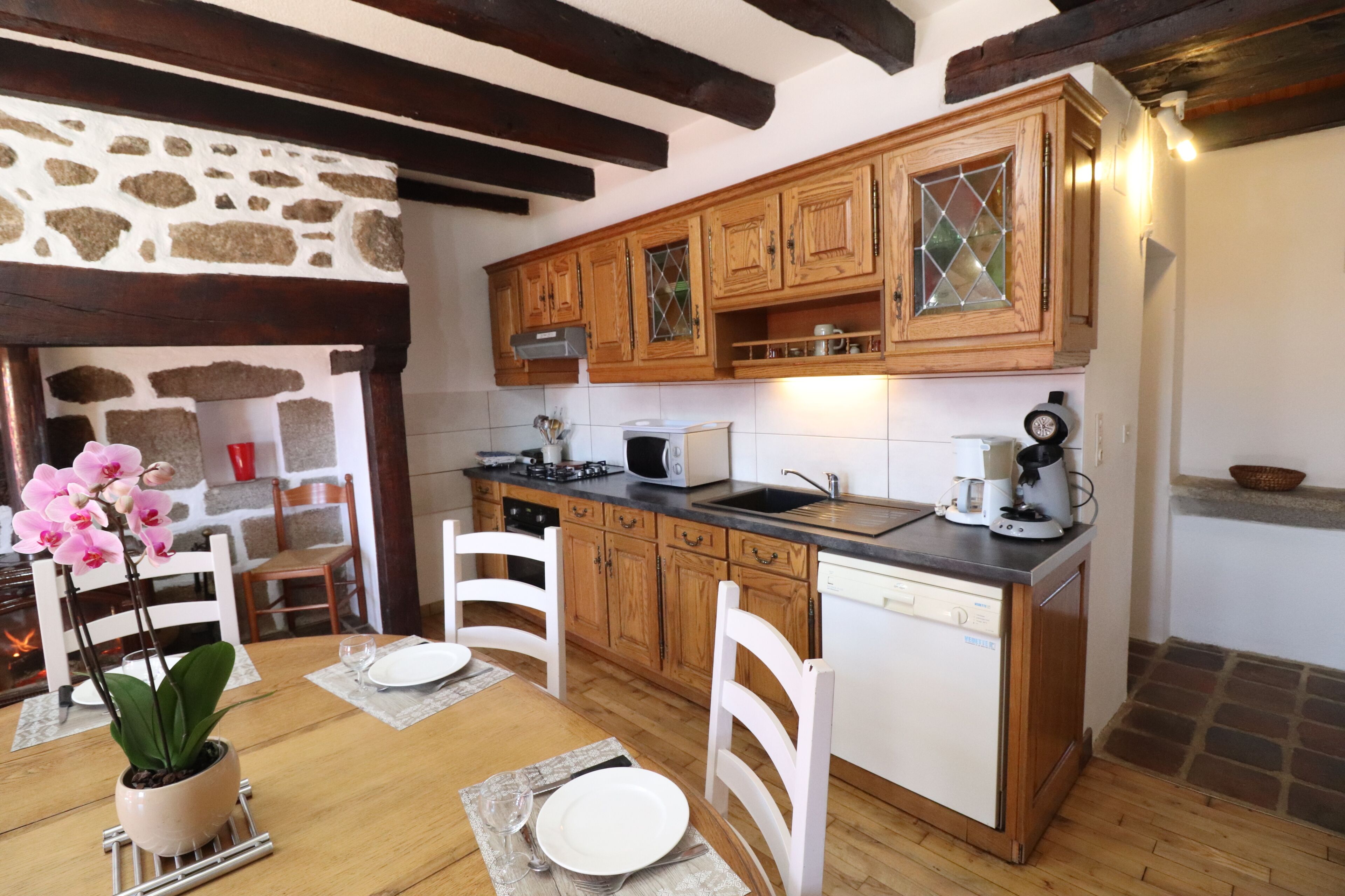 A kitchen with wooden cabinets, a microwave, a sink, and a dining area with chairs and a table.