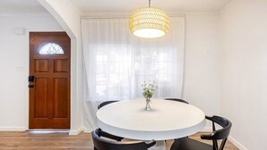 A dining area with a round table, black chairs, a hanging light fixture, a wooden door, and a window with sheer curtains. - Furnished 3BR in Tracy, Comfortable longer stays (Tracy)