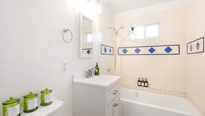 A bathroom with a white sink, mirror, and bathtub. There are three green bottles on the sink and two on the wall. - Furnished 3BR in Tracy, Comfortable longer stays (Tracy)