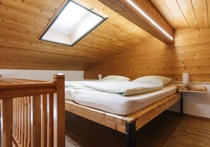 Ein Zimmer mit Holzboden, einem Bett, einem Dachfenster und einem Nachttisch.