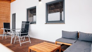 En modern utomhusplats med sittmöbler, bestående av ett träbord, en soffa och en stol.