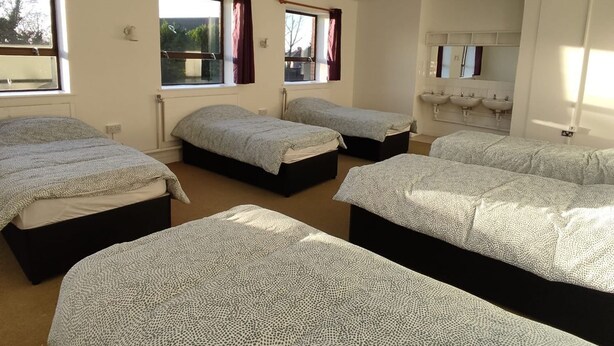 Ein Zimmer mit vier Betten, einem Badezimmer mit zwei Waschbecken und Fenstern mit Vorhängen.