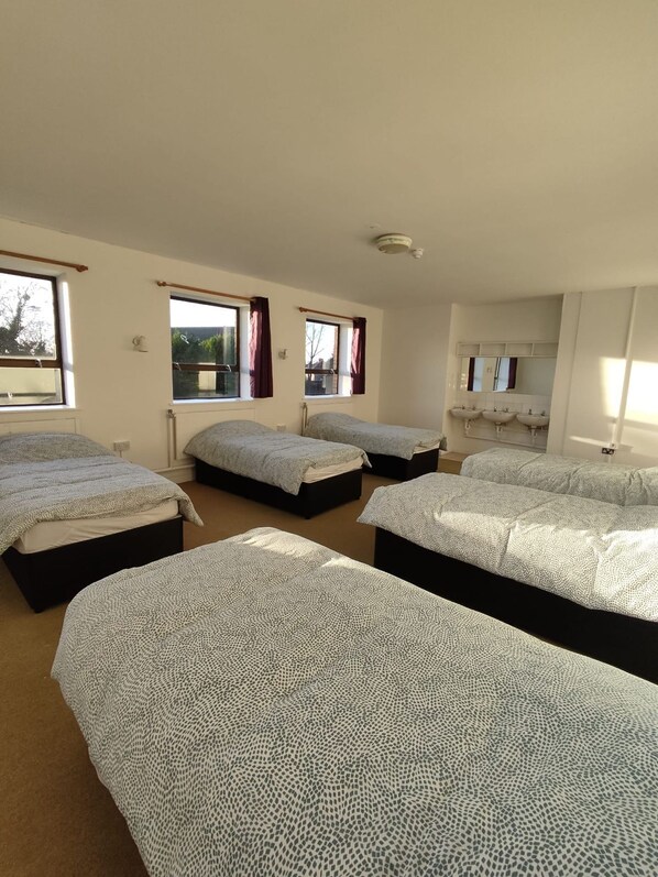 Una habitación con cuatro camas, un baño con dos lavamanos y ventanas con cortinas.