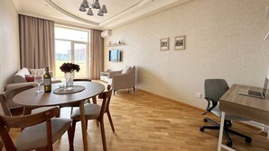 A modern living room with a dining area, a sofa, a TV, and a desk with a laptop. - Playstation 5 + Panoramic City view Apartment (Baku)