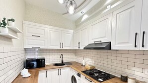 A modern kitchen with white cabinets, a black stove, a sink, and a microwave. - Playstation 5 + Panoramic City view Apartment (Baku)