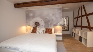 A bedroom with a large bed, bedside tables, a mirror, and a wooden ceiling beam. - Ferienwohnung für 4 Personen in Suhl (Suhl)