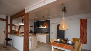 A modern kitchen with wooden beams, a central island, bar stools, and a dining area with a table and chairs. - Ferienwohnung für 4 Personen in Suhl (Suhl)