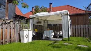 A covered outdoor seating area with a table and chairs, a white tent, and a garden with a wooden fence. - Ferienwohnung für 4 Personen in Suhl (Suhl)