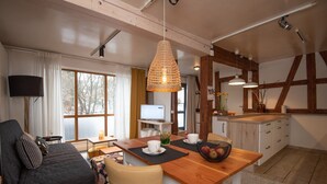 A modern kitchen with wooden beams, a dining table with white chairs, and a TV. - Ferienwohnung für 4 Personen in Suhl (Suhl)
