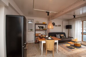 A modern living room with a black refrigerator, wooden dining table, and a sofa.