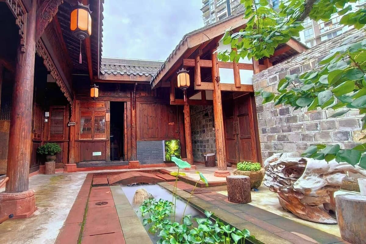 A traditional wooden courtyard with a water feature, stone lanterns, and a rustic seating area.