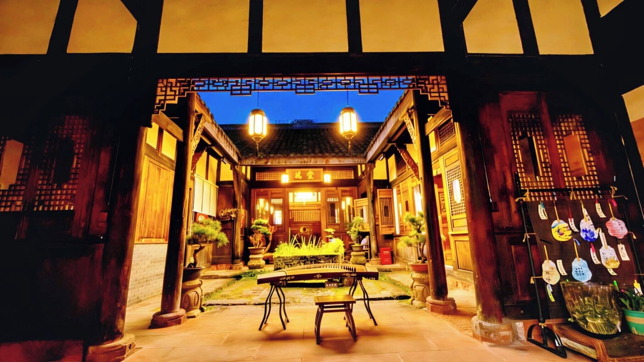 A traditional wooden building with a tiled roof, a central courtyard with a table and chairs, and a decorative gate.