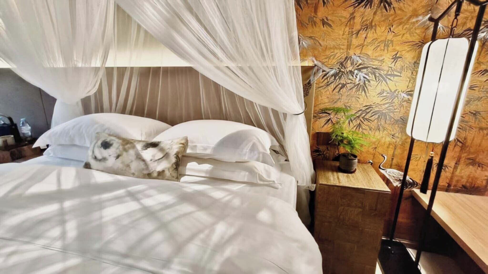 A bed with a canopy, a bedside table with a lamp, and a wall with a bamboo pattern.