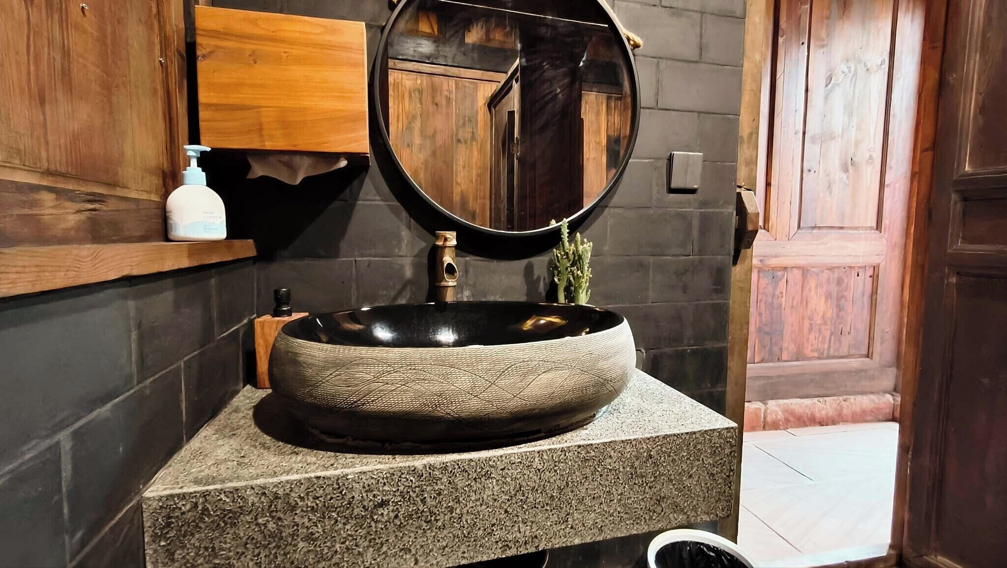 A bathroom with a round, textured sink, a wooden cabinet, and a mirror.