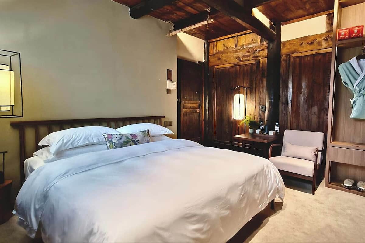 A bedroom with a bed, a chair, a wooden wardrobe, and a hanging robe.