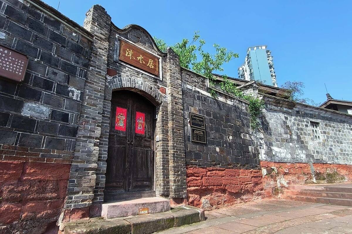 A historic building with a traditional Chinese architectural style, featuring a stone wall, a wooden door with red decorations, and a signboard.