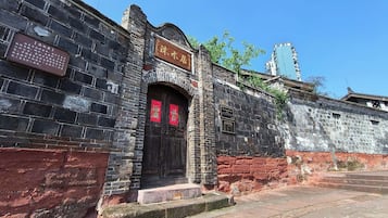Un edificio histórico con arquitectura china tradicional, que presenta un muro de piedra, una puerta de madera con adornos rojos y un letrero.
