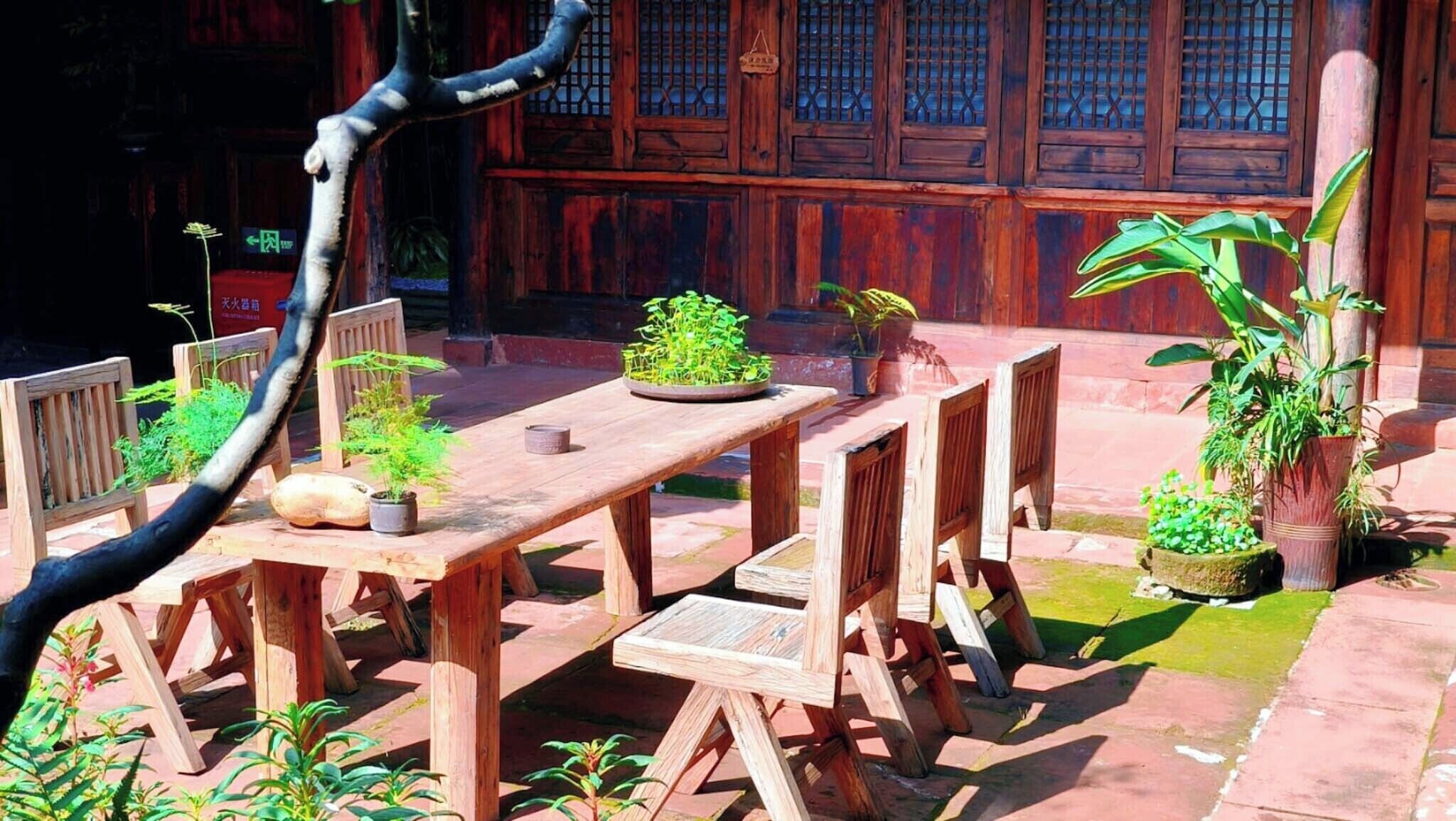 A wooden table and chairs set outdoors with potted plants and a traditional wooden building in the background.