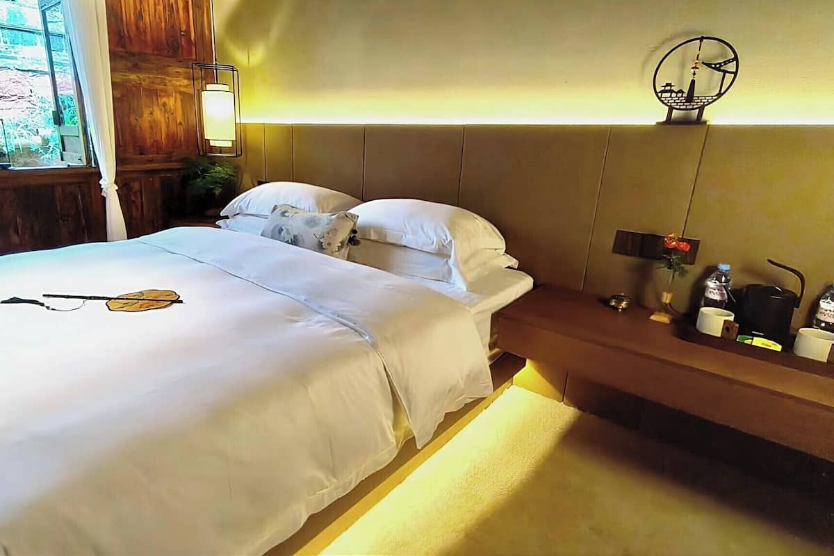 A hotel room with a bed, bedside table, lamp, and a view of the outdoors.