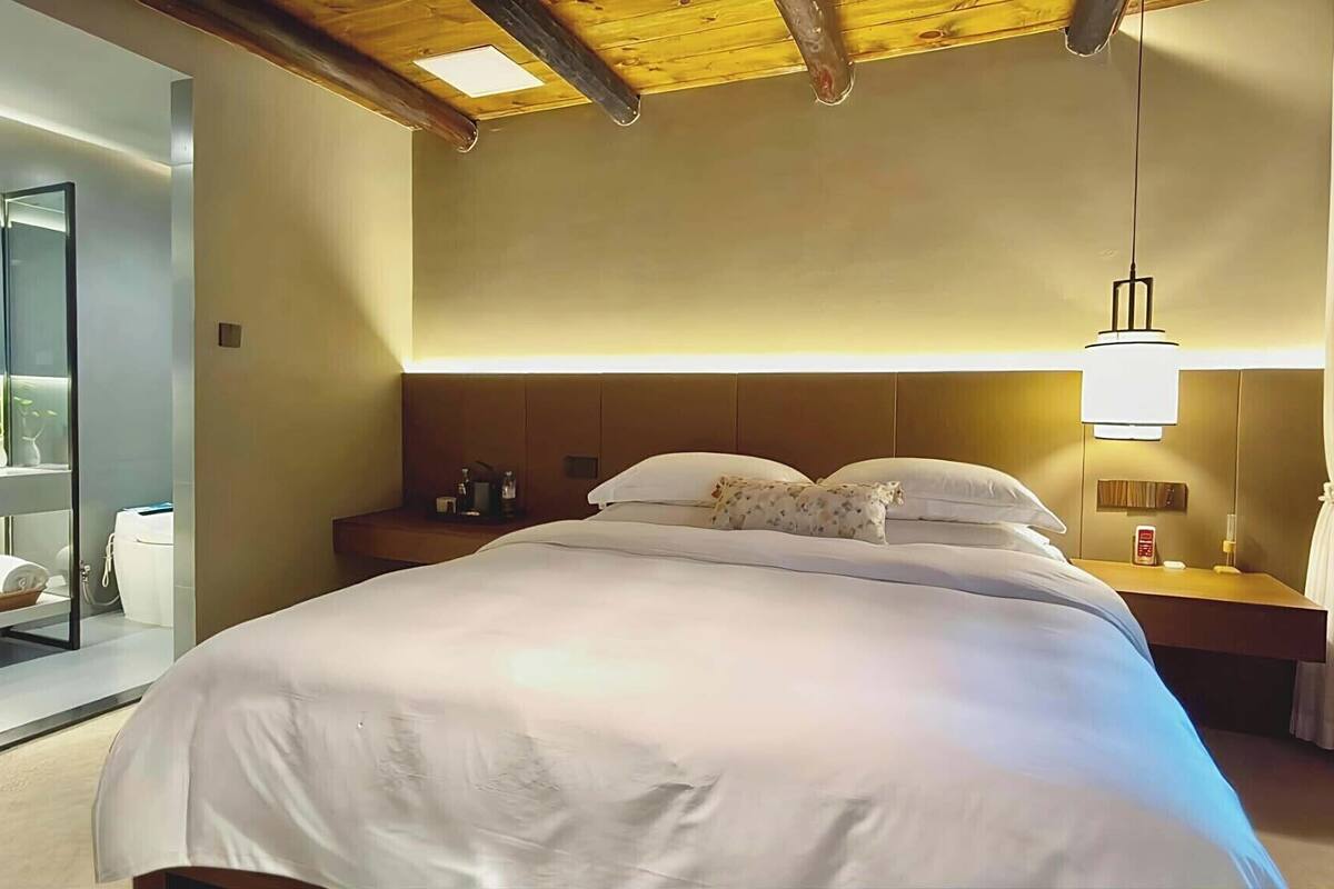 A hotel room with a large bed, bedside tables, a nightstand, a mirror, and a ceiling light fixture.