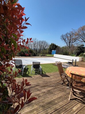 En træterrasse med udendørs møbler, en pool og udsigt over det omkringliggende landskab.