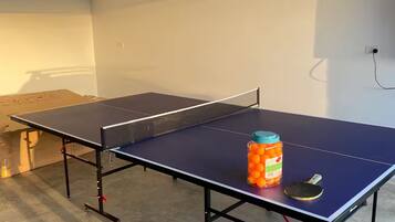 A ping pong table with a jar of oranges and a paddle in a room with a concrete floor and a white ceiling.