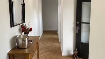 A hallway with a wooden bench, a metal bucket, a decorative mirror, and a wicker pendant light.