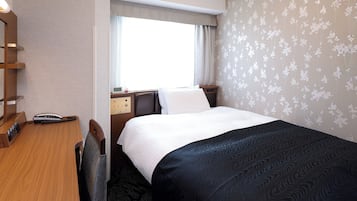 A hotel room with a bed, a desk with a telephone, a bedside table with a clock, and a window with curtains.
