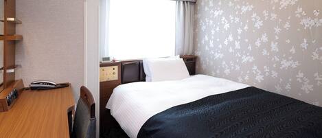 A hotel room with a bed, a desk with a telephone, a bedside table with a clock, and a window with curtains.