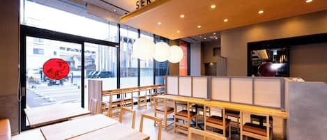 Interior de restaurante con mesas y sillas de madera, un cartel de servicio y vistas a la calle.