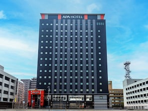 Un hôtel moderne, reconnaissable à son grand panneau « APA HOTEL » placé en haut de l’immeuble.