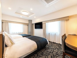 Habitación de hotel con cama, escritorio, silla, televisión y ventana con cortinas.