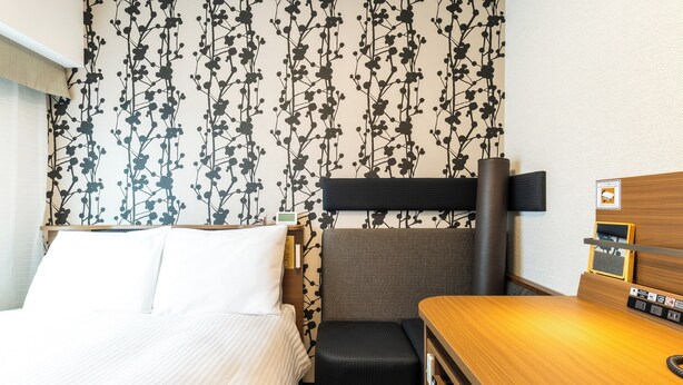 Ein Hotelzimmer mit einem Bett, einem kleinen Schreibtisch, einem Sessel und einer Wand mit floralem Muster.