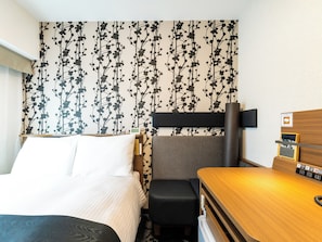 Une chambre d’hôtel avec un lit, un petit bureau, une chaise et un mur orné d’un motif floral.