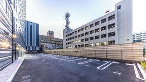 Ein Parkplatz mit markierten Stellplätzen, ein Gebäude mit P-Schild und ein Mobilfunkturm im Hintergrund.