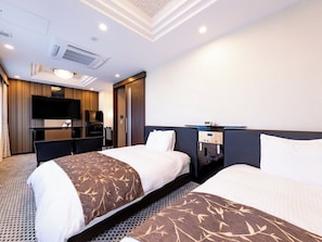 Une chambre d’hôtel avec deux lits, un bureau, un téléviseur à écran plat, un minibar et un plafond doté d’un éclairage encastré.