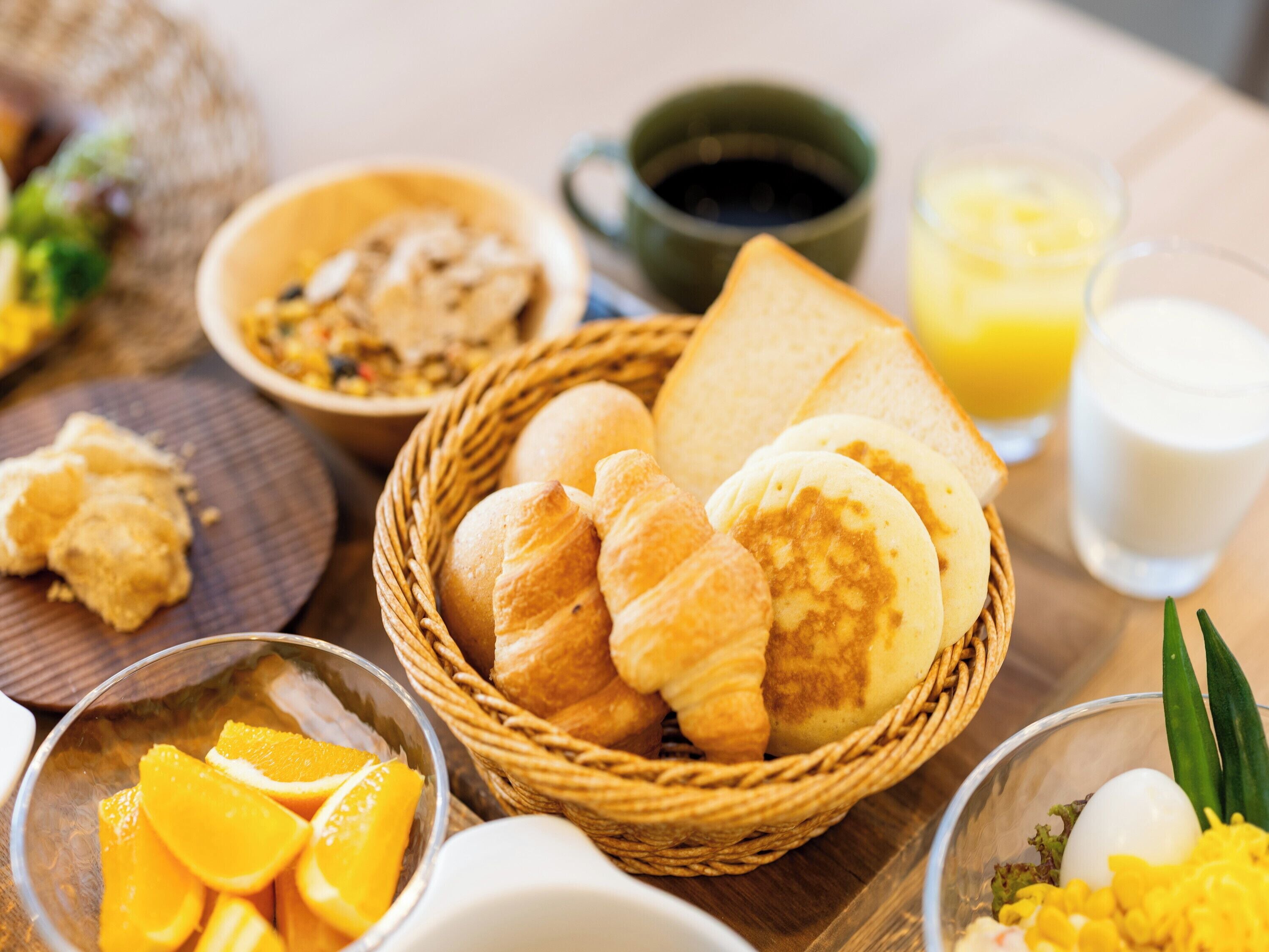 Una mesa con desayuno que incluye pan, bollería, fruta y bebidas.