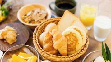 Una mesa con desayuno que incluye pan, bollería, fruta y bebidas.