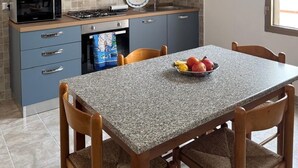 Een keuken met grijze kastjes, een magnetron, een gasfornuis en een eettafel met stoelen.