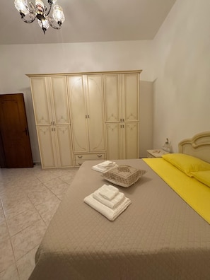 Un dormitorio con cama, armario, mesita de noche y araña.