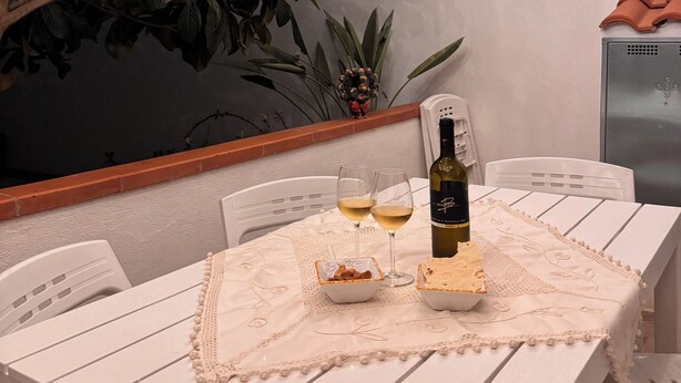 Een witte tafel met een fles wijn, twee glazen en een klein bordje eten.