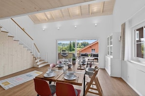 A spacious dining area with a view of the outdoors, a wooden staircase, and a large window with curtains. - Large gallery apartment with balcony, home cinema, garden, centrally located in the Allgäu (Sulzberg)
