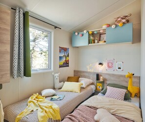 Ein gemütliches Schlafzimmer mit zwei Betten, einem Fenster mit Vorhängen, einer Wand mit einem Poster und einem Regal mit Spielzeug.