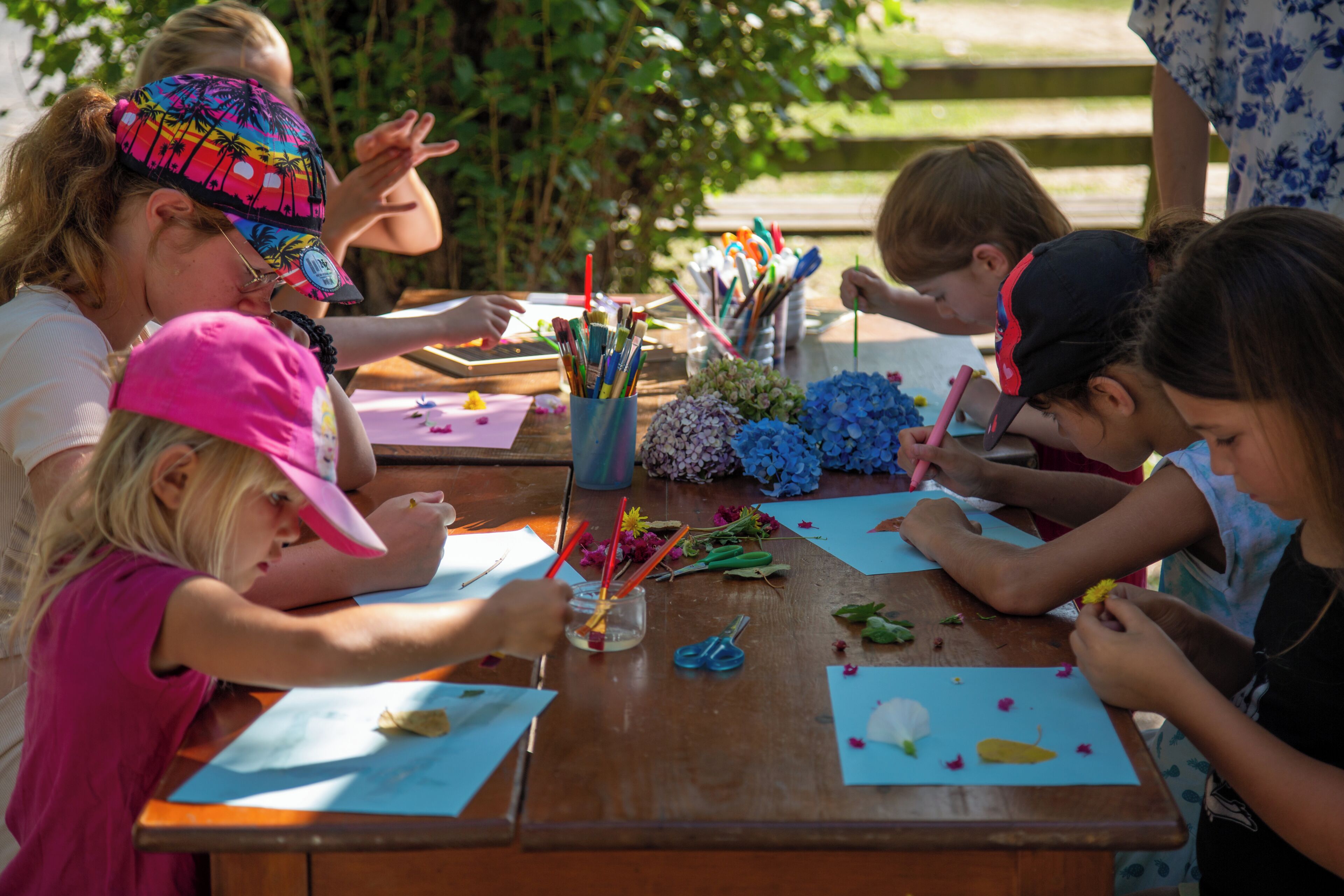 A group of people engaged in a craft activity at a wooden table with art supplies and paper.