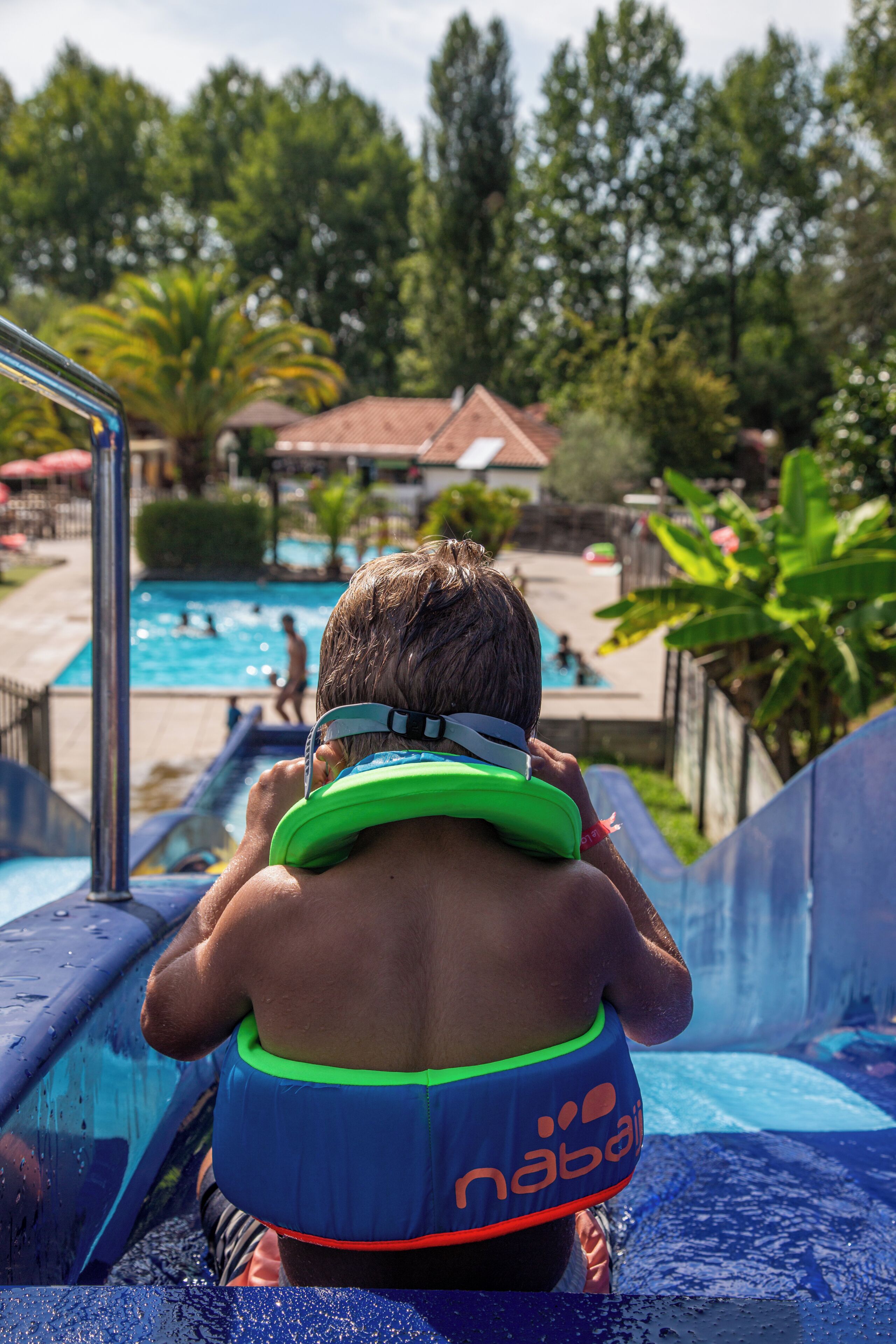 Uma pessoa em um tobogã aquático com um dispositivo de flutuação, água e uma piscina ao fundo.