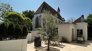 A courtyard with a church, a planter with a tree, and a planter with plants.
