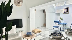 A modern living room with a flat-screen TV, a dining area with blue chairs, a round table, and a hanging light fixture. - Zina apartment Sidi Bou Saïd (Sidi Bou Said)