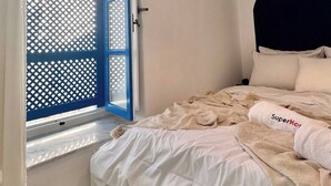 A bedroom with a bed, a window with a blue frame, a wicker light fixture, and a white headboard. - Zina apartment Sidi Bou Saïd (Sidi Bou Said)